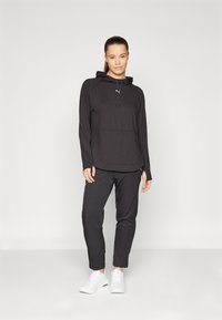 Svart sportig hoodie med dragsnören, långa ärmar och framficka, matchad med svarta tapered byxor och vita träningsskor.
