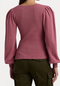 Pletený svetr v jemně růžové barvě, s ribbením, kulatým výstřihem a balónovými dlouhými rukávy. Spárován s olivově zelenými kalhotami.