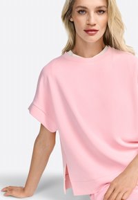 Světle růžové oversized tričko s krátkými ohrnutými rukávy a kulatým výstřihem, se bočními rozparky a hladkým bavlněným materiálem.