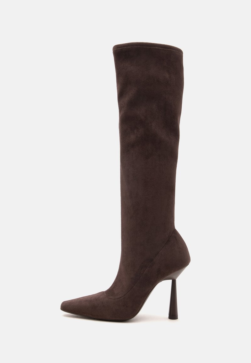Botte haute en daim brun foncé à bout pointu avec un talon haut étroit, debout droite sur un fond clair uni.