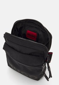 Borsa nera in nylon con chiusura a zip. Esterno morbido e imbottito con un'etichetta rossa all'interno e cuciture a contrasto. Accessori in hardware durevole.