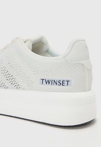 Hvit perforert sneakers med teksturert mesh-overdel, tykk hvit såle og svart "TWINKSET"-logo på hælflappen.