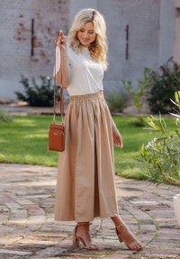 Light-colored top paired with a beige, pleated midi skirt. Includes a small brown crossbody bag and light heeled sandals. Natural background.