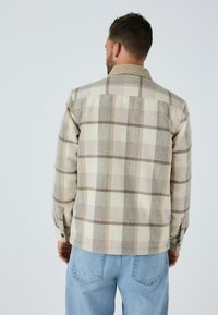 Beige- und braun kariertes Hemdjackett mit einem Sherpa-Kragen, langen Ärmeln und Knopfmanschetten, aus einem strukturierten Stoff gefertigt.