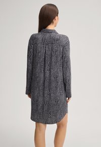 Langes Shirt aus schwarzem Stoff mit einem weißen strukturierten Krokodilhautmuster. Verfügt über einen Kragen, lange Ärmel und einen leicht geschwungenen Saum.