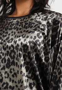 Top s leopardím vzorem vyrobený z lesklé metalické látky v černých a šedých odstínech, s volným střihem a kulatým výstřihem.