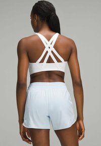 Sujetador deportivo blanco con tirantes en forma de cruz en la espalda, combinado con pantalones cortos deportivos de color azul claro que cuentan con una cinturilla elástica y aberturas laterales.
