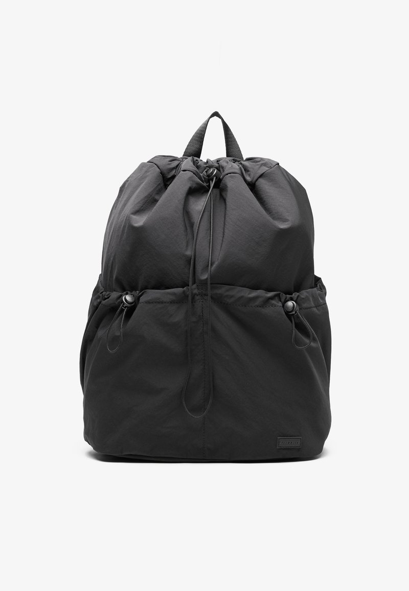 Mochila negra con cordón, de textura suave, con forma redondeada, bolsillos laterales y cierres de plástico. La tela parece ligera.