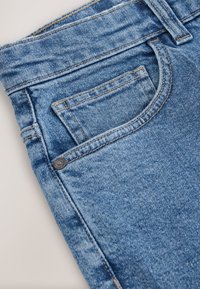 Jeans in denim azzurro chiaro con tasca anteriore, dettagli cuciti e bottone in metallo sulla vita. La texture appare leggermente consumata.