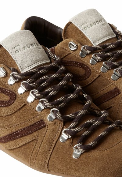 Scarpe in suede marrone con accenti beige, lacci rotondi in marrone scuro e crema, occhielli metallici e una superficie superiore morbida e testurizzata.