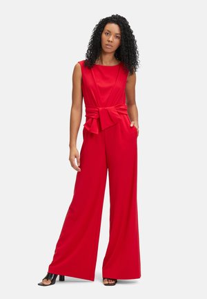 Combinaison rouge avec jambes larges, en tissu lisse, corsage ajusté et accent nœud à l'avant. Comprend des poches latérales et un design sans manches.