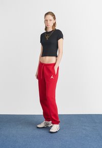 Czerwone dresy z elastycznym pasem i bocznymi kieszeniami, z białym logo. W zestawie z czarnym krótkim t-shirtem i trampkami.