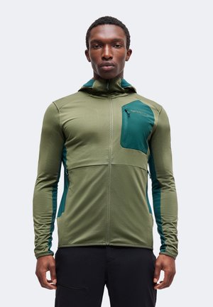 Homme athlétique portant une veste zippée verte et bleu sarcelle avec capuche et un pantalon noir, debout avec les bras détendus le long du corps.