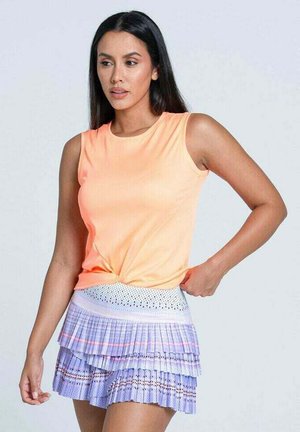 Helles orangefarbenes ärmelloses Top, das an der Taille geknotet ist, kombiniert mit einem plissierten fliederfarbenen Rock mit gestuften Rüschen und einem gemusterten Taillenband.