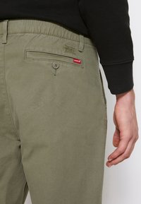 Olivegröna byxor gjorda av kraftigt tyg, med elastisk midja, bakficka med knappstängning och en liten röd Levi's-logotyp.