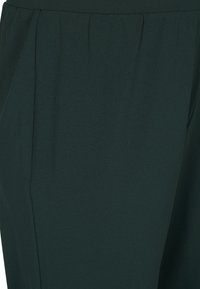 Tissu lisse vert foncé présentant une coupe décontractée. Comprend des plis au niveau de la taille pour ajouter de la texture et de la dimension.