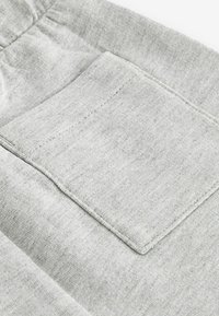 Tissu gris clair avec une texture douce présentant une poche carrée. Les coutures visibles ajoutent du détail, et la taille est légèrement froncée.