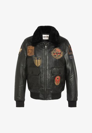 Veste bomber en cuir noir avec un col en fausse fourrure, comportant plusieurs patches colorés et texturés sur le devant et les manches.