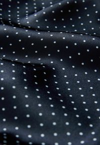 Tejido de satén azul marino con textura suave, presenta lunares blancos espaciados uniformemente, creando un patrón sutil en la superficie.