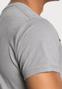 Close-up of a person's upper arm and shoulder wearing a light grey short-sleeve shirt with visible seam stitching.