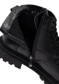Zwarte leren enkelboot met een gestructureerde afwerking, zichtbare veters en een zipper aan de zijkant. Dikke rubberen zool met een geribbeld patroon voor grip.