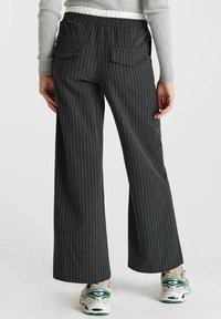 Pantalons à large jambe à rayures noires avec une taille élastique et deux poches arrière, associés à des baskets blanches. Le tissu a une texture douce.