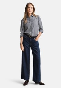 Striped button-up shirt in navy and white, paired with high-waisted dark denim wide-leg pants, accentuated by a black belt and brown boots.