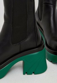 Botines de cuero negro con un tacón grueso texturizado en verde, paneles laterales elásticos y un acabado suave.