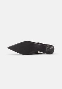 Semelle de chaussure noire à bout pointu avec une surface antidérapante texturée, vue de dessous sur un fond clair uni.