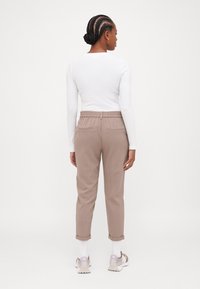 Ljust färgad långärmad topp kombinerad med beige, avsmalnande byxor med elastisk midja och två bakfickor, visad bakifrån.