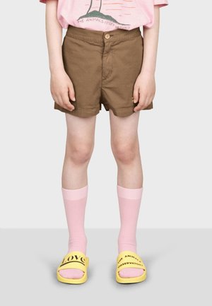 Shorts en coton marron avec un bouton sur le devant, chaussettes roses jusqu'aux genoux et sandales jaunes à glisser avec le mot "AMOUR" en noir.