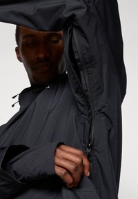 Chaqueta negra con ventilación lateral con cremallera y mangas alargadas con agujeros para los pulgares, fabricada en una tela suave y ligera.