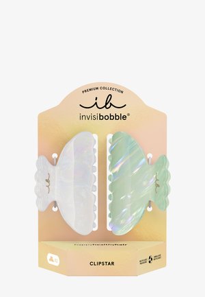 Dos pinzas de pelo iridiscentes, una blanca y otra verde claro, mostradas en una tarjeta de la colección premium Invisibobble Clipstar de color melocotón.
