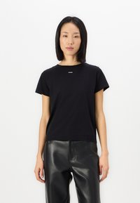 Μαύρο κοντομάνικο βαμβακερό t-shirt με στρογγυλή λαιμόκοψη και μικρό λευκό λογότυπο στο στήθος, συνδυασμένο με μαύρο δερμάτινο παντελόνι.