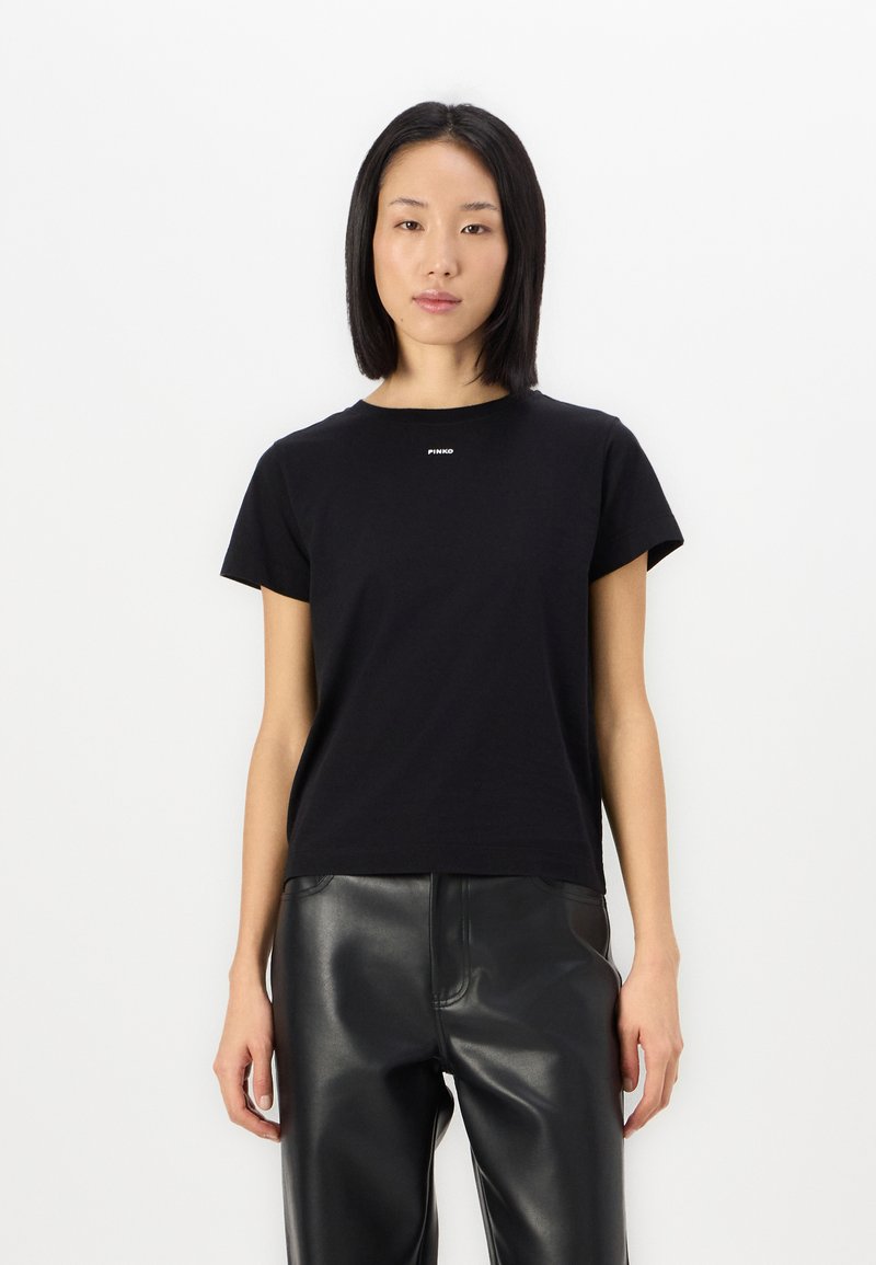 Μαύρο κοντομάνικο βαμβακερό t-shirt με στρογγυλή λαιμόκοψη και μικρό λευκό λογότυπο στο στήθος, συνδυασμένο με μαύρο δερμάτινο παντελόνι.