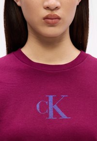 Βουργουνδίνα βαμβακερή μπλούζα με στρογγυλή λαιμόκοψη που διαθέτει μπλε κεντητό λογότυπο "CK" στην μπροστινή πλευρά. Λείο υλικό, χαλαρός σχεδιασμός.