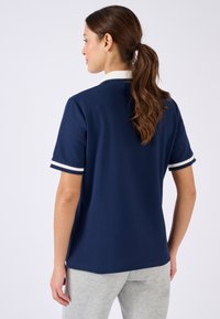 T-shirt polo bleu marine à manches courtes, avec des accents rayés blancs au niveau des poignets et un col blanc. Texture lisse et coupe décontractée.