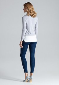 Lichtgrijze lange mouw top met witte onderlaag, gecombineerd met donkerblauwe skinny jeans en lichtgrijze hoge hakken. Minimalistisch ontwerp.
