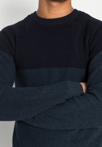 Strickpullover mit strukturiertem Muster in dunkelblauen und aquafarbenen horizontalen Streifen. Rippstrickbündchen an den Ärmelenden und am Kragen sorgen für eine eng anliegende Passform.