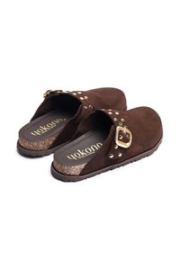Sabots en daim marron à enfiler avec semelles en liège, boucle dorée et détails en clous, marqués "Yokono" à l'intérieur.