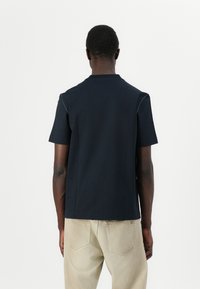 Camiseta de manga corta azul marino de algodón, con un cuello redondo y costuras contrastantes en las costuras de los hombros. Diseño sencillo.
