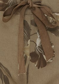 Brunt blomsterstof med en struktureret overflade, der har et bundet bånd i taljen og store blomster mønstre i dæmpede nuancer.