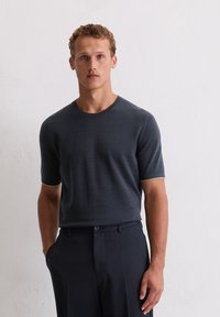 Ciemnoniebieska, krótko rękawowa koszulka dzianinowa z okrągłym dekoltem i jasnoniebieskimi wykończeniami przy mankietach, w połączeniu z dopasowanymi ciemnymi spodniami.