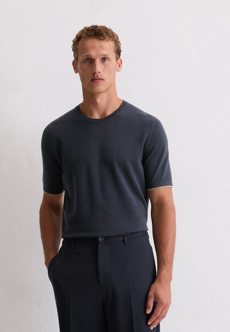 Ciemnoniebieska, krótko rękawowa koszulka dzianinowa z okrągłym dekoltem i jasnoniebieskimi wykończeniami przy mankietach, w połączeniu z dopasowanymi ciemnymi spodniami.