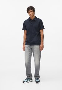 Granatowa polo z teksturą, krótkie rękawy, z kołnierzykiem. Połączona z wyblakłymi szarymi dżinsami i trampkami z niebieskimi akcentami.