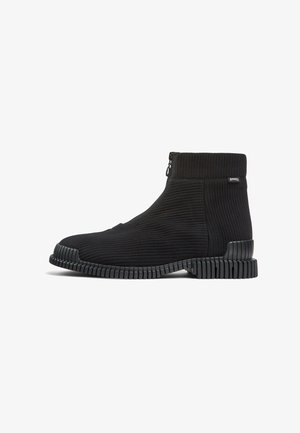 Schwarze Knöchelstiefel mit einem gerippten Textilobermaterial, seitlichem Reißverschluss und einer strukturierten Gummisohle mit horizontalen Rillen.