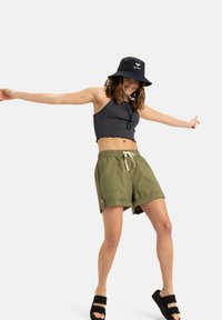 Svart ribbad cropped topp med scalloped nederkant, olivgröna shorts med dragsko, svart bucket hat med logotyp, och svarta slidesandaler.