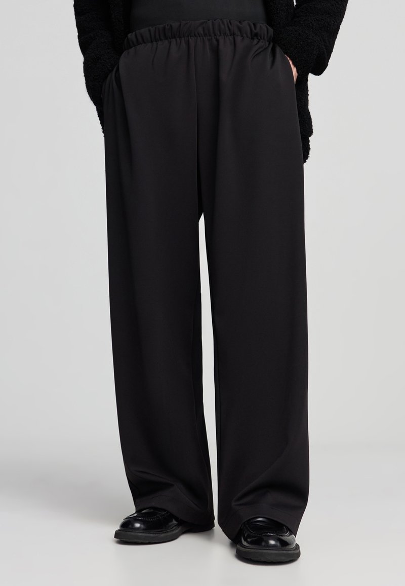 Pantaloni neri a gamba larga realizzati in tessuto morbido, con una vita elastica per il massimo comfort. Texture liscia senza pattern o accenti visibili.