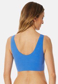 Crop top bleu sans couture avec de larges bretelles et un dos en U. Fabriqué à partir d'un matériau doux et extensible, présentant une texture lisse et des coutures minimales.