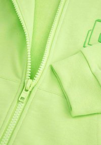 Neonowa zielona bluza z zamkiem błyskawicznym, z fakturowanym wewnętrznym wykończeniem, ściągaczami na rękawach i pasującymi detalami na zamku. Gładki materiał i nowoczesny design.